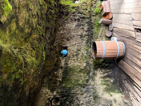       Mossy cave interior with an old wooden barrel and a blue teapot fixed to the rock wall
  