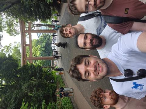       Friends take a selfie beneath a large wooden torii gate in a forested shrine approach.
  