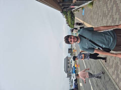       Traveller poses at a windy overlook with a faint silhouette of Mount Fuji in the clouds.
  