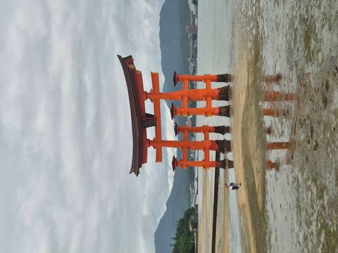       Iconic orange torii gate of Itsukushima Shrine standing in shallow coastal waters with mountain backdrop.
  