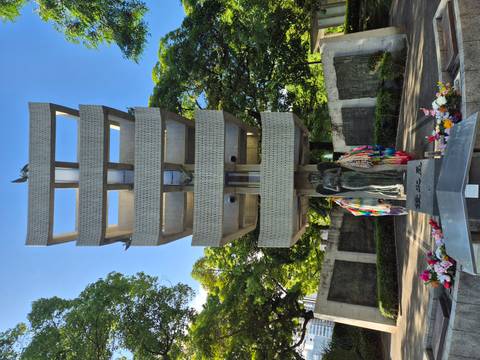       Memorial tower and statues adorned with folded paper cranes in a peaceful park.
  