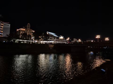      Bridge and riverside buildings softly lit and reflected on water in the dark night.
  