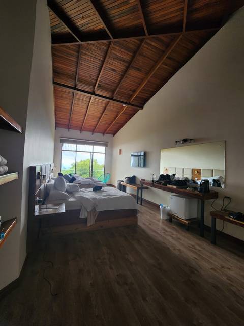       Spacious hotel room with high wooden ceiling, unmade bed, and large window overlooking cloud forest.
  