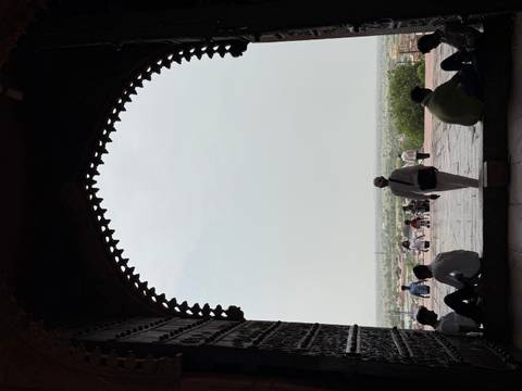       Silhouetted visitors framed by a massive arched gateway look out over Fatehpur Sikri plains.
  