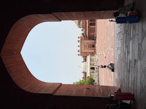       View through an arched corridor onto Fatehpur Sikri’s central square and white marble shrine.
  