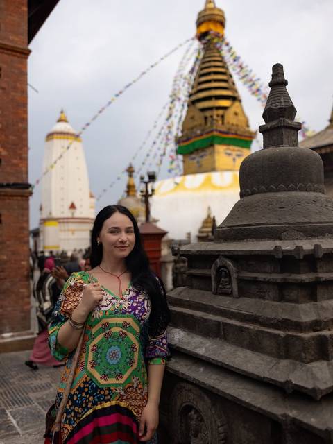       Female traveller posing in front of a white Buddhist stupa draped with prayer flags.
  