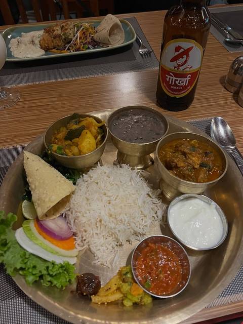       Traditional Nepali thali plate with rice, assorted curries, lentils and yogurt served in brass bowls.
  