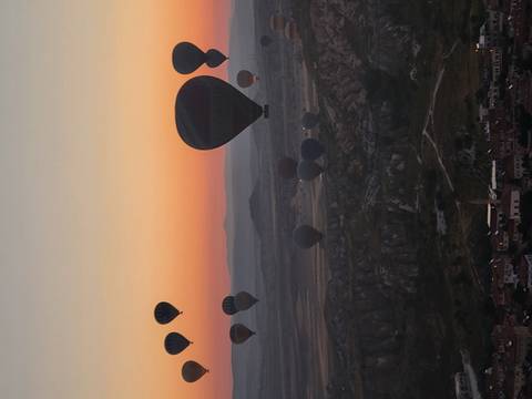       Dozens of hot-air balloons rise over a rocky plateau at dawn, silhouetted against orange sky.
  