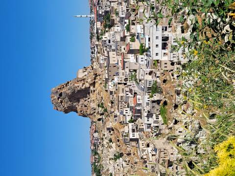       Rock citadel towers above a sprawling Cappadocia village on a bright summer day.
  