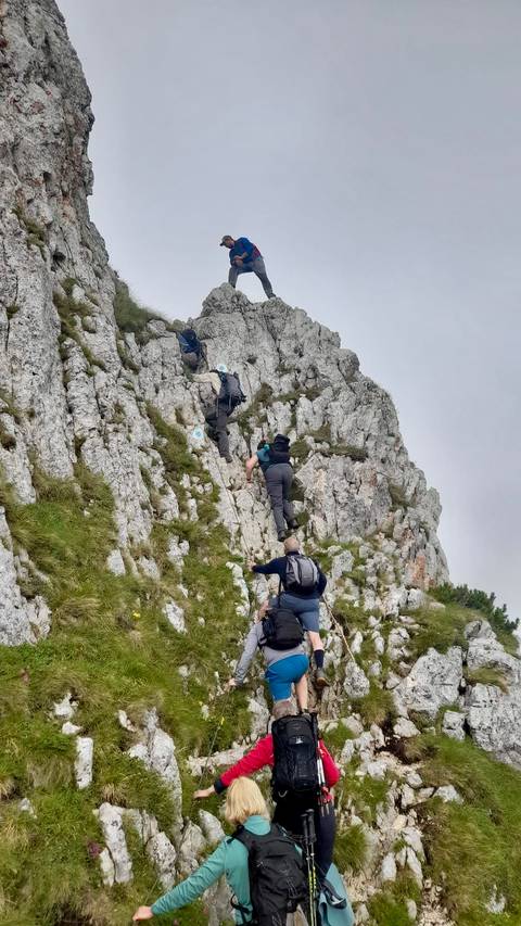       Hikers climbing steep jagged limestone ridge using hands for support
  