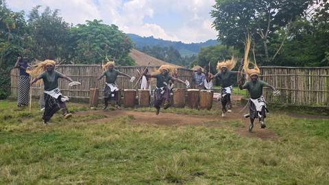       Traditional Rwandan dancers leap high with straw headdresses while drummers play behind them.
  