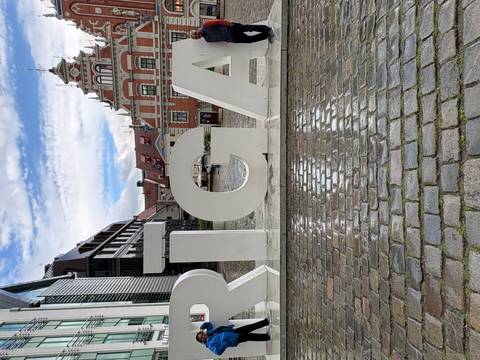       Large white "RIGA" letters stand on a wet cobblestone square with historic buildings behind.
  