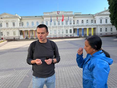      Local guide explains history to a visitor outside a neoclassical government building in Vilnius.
  