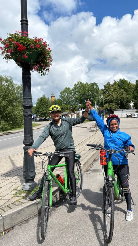       Two cyclists celebrate holding hands beside their bikes on a small town street.
  