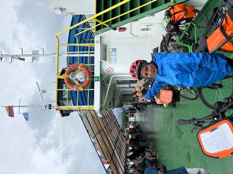       Traveller in blue rain jacket points while standing aboard a bicycle ferry deck.
  