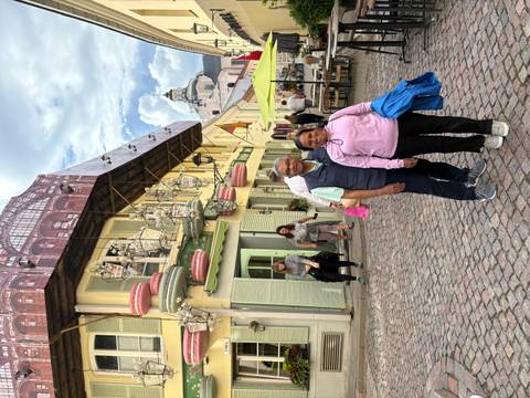       Couple stands on a cobblestone street lined with colourful historic buildings and outdoor cafés.
  