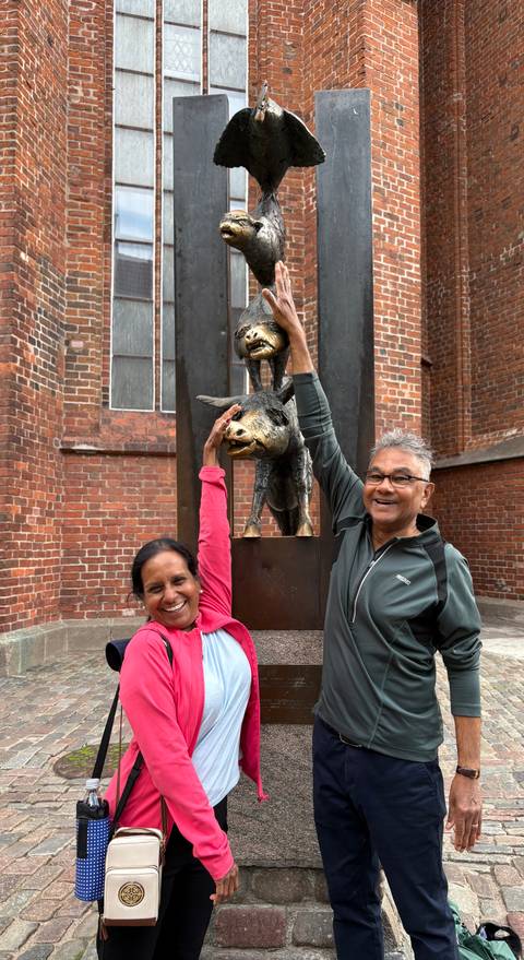       Travellers playfully reach for the Bremen Town Musicians bronze statue against a brick church wall.
  