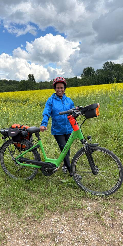       Cyclist pauses with a green bike beside a vibrant yellow rapeseed field and tall grass in the countryside.
  