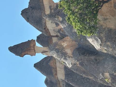       A tall fairy-chimney rock formation with a mushroom cap stands against a bright blue sky in Pasabag.
  