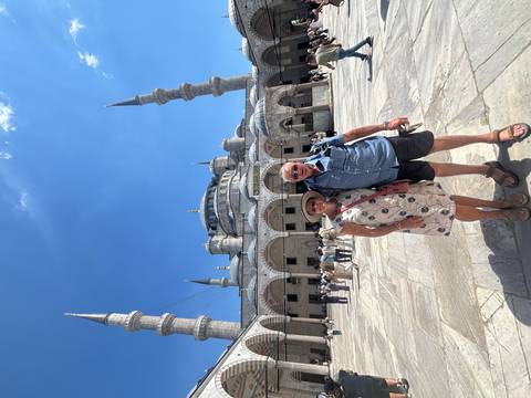       A smiling couple stands in the courtyard of Istanbul’s Blue Mosque beneath its elegant minarets.
  