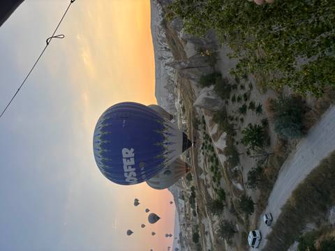       A blue hot-air balloon hovers low over rugged Cappadocia terrain at sunrise.
  