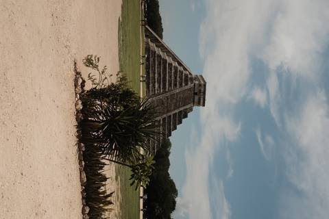       Iconic El Castillo pyramid at Chichen Itza rising against a blue sky with visitors nearby.
  
