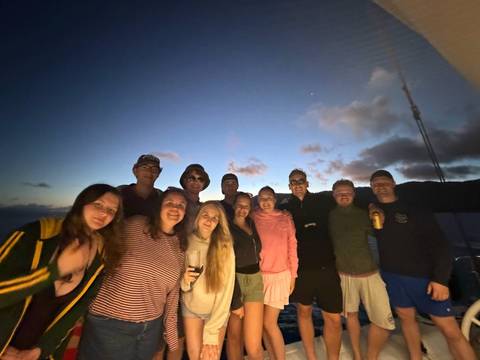       Evening group photo on boat deck with twilight sky in background
  