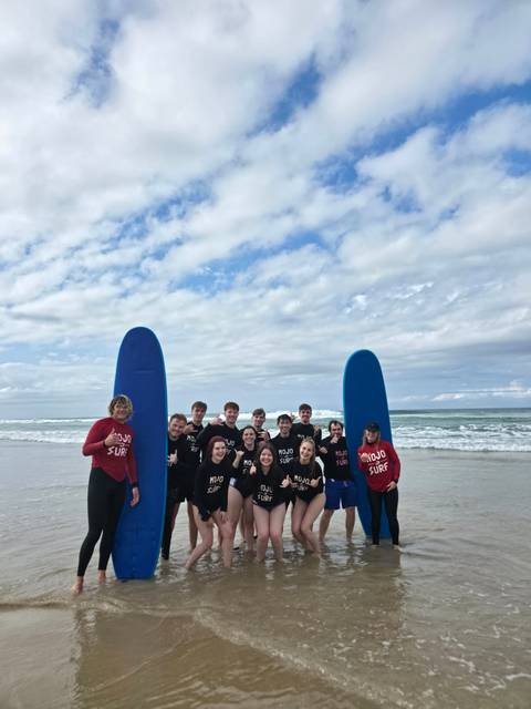       Surf school group in wetsuits poses with blue surfboards on cloudy beach
  
