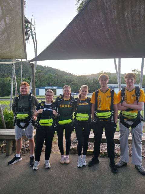       Young travellers in skydiving harnesses stand smiling at small airport
  