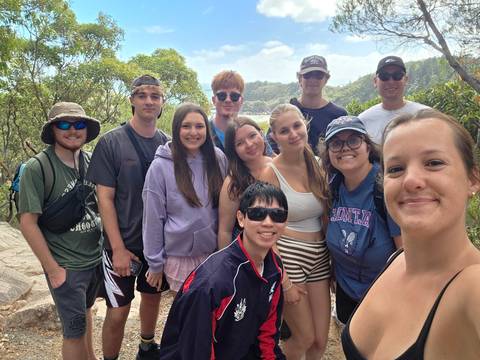       Hiking group poses on rocky viewpoint surrounded by lush tropical foliage
  