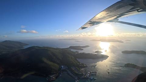       Aerial view of island-studded sea from plane wing with bright sun reflection
  
