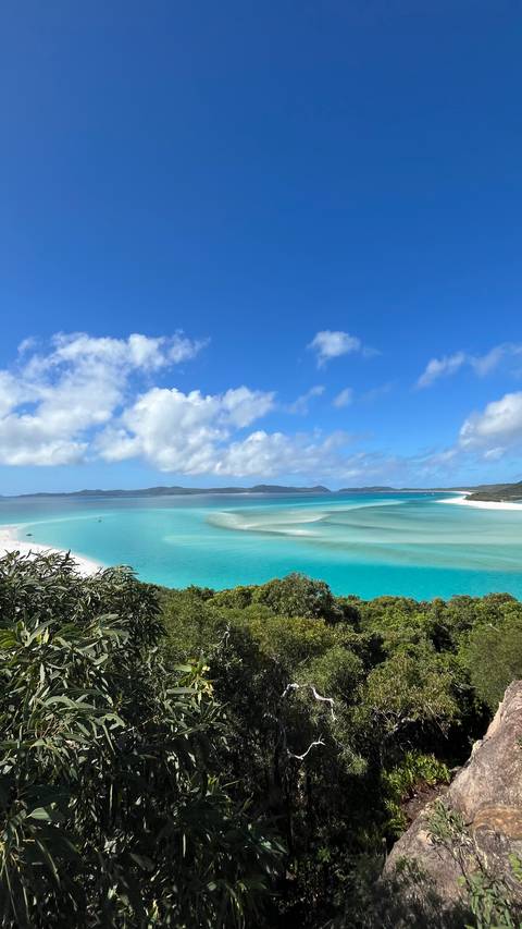       Panoramic view over Whitehaven Beach with swirling white sand bars and vivid turquoise water under a blue sky
  