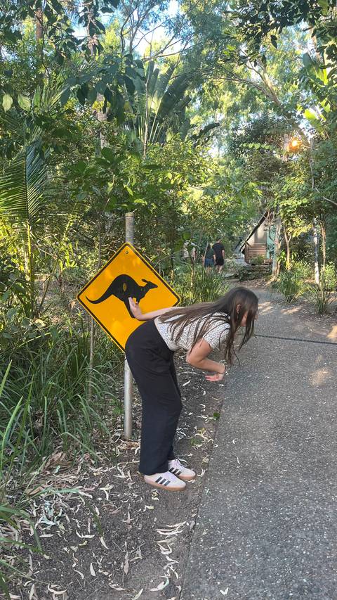       Woman playfully posing beside a yellow kangaroo crossing sign on a forest path
  