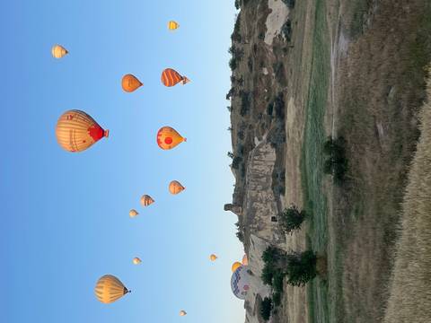       Dozens of colorful hot-air balloons rise over Cappadocia’s rocky landscape beneath a clear dawn sky.
  
