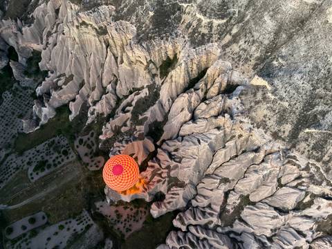       Top-down aerial of a single orange balloon drifting above Cappadocia’s rippled rock landscape.
  