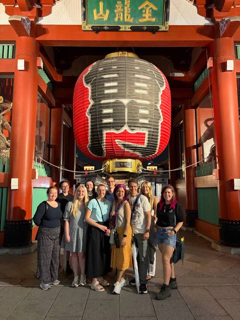       Tour group poses beneath the giant red lantern at the gate of Senso-ji Temple in Tokyo.
  