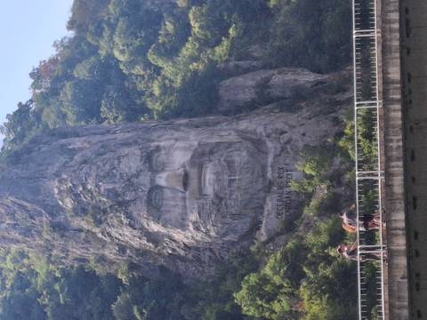       Towering rock carving of Decebalus’s face overlooks the Danube gorge as tourists cross a bridge below.
  