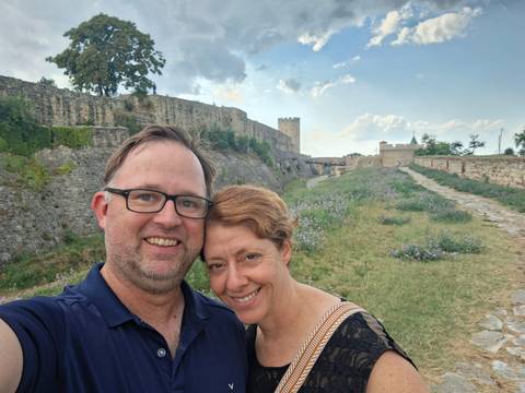       Couple poses on a grassy rampart with the ancient stone walls and towers of Belgrade Fortress in the background.
  