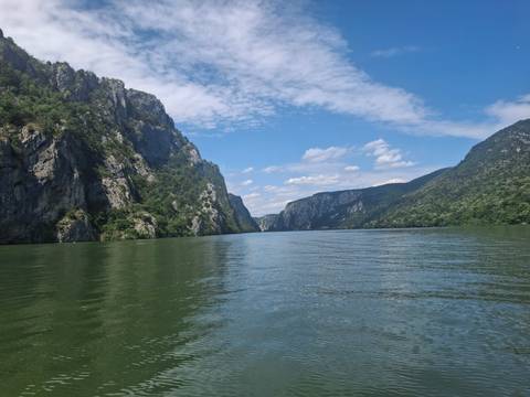       Scenic river gorge with steep forested cliffs and calm green water under a bright blue sky.
  