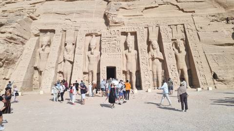       Crowds gather in front of the colossal statues and hieroglyphs carved into the facade of Abu Simbel Temple.
  