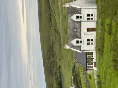       White stone cottage set amid rolling green moorland under a cloudy sky.
  