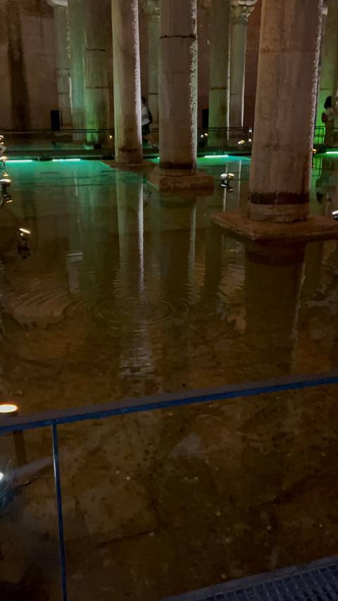       Dimly lit underground pool with rippling water reflecting stone columns.
  