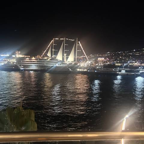       Night view of an illuminated cruise ship and harbour lights reflecting on dark water.
  