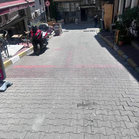      Sun-drenched cobblestone street with red painted arrows, a motorcycle and café terrace tables.
  