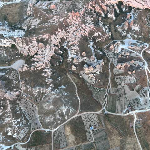       Drone view of Cappadocia’s pink-hued rock spires, trails and patchwork orchards after snowfall remnants.
  