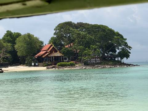       A small tree-covered island with a Thai pavilion sits offshore in calm jade-green sea.
  
