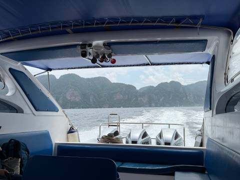       View from the back of a speedboat leaving a foamy wake toward towering green limestone cliffs.
  