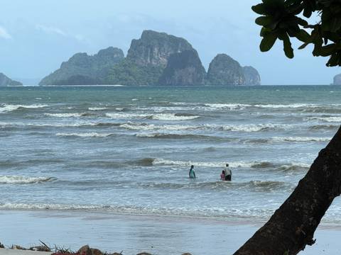       Two people wade in choppy shallows with rugged limestone islands rising beyond a wind-ruffled sea.
  