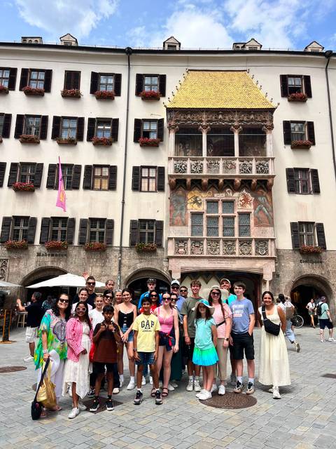       A large tour group poses in front of Innsbruck's ornate Golden Roof façade.
  