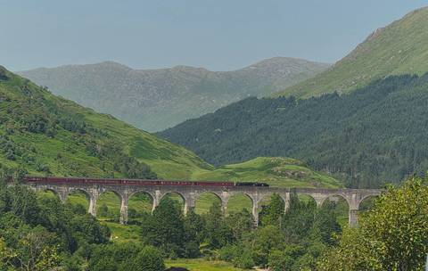       Historic Glenfinnan Viaduct carries a red steam train through lush green Highland scenery.
  